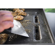 Reinigung einer Grillplatte mit einem Schaber und Essensresten