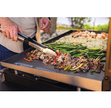 Grillplatte mit Fleisch, Gemüse und Reis wird mit einer Grillzange gewendet.