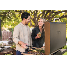 Zwei Personen grillen im Freien mit einem Tepro Grill und Grillzange, eine Frau hält ein Getränk.