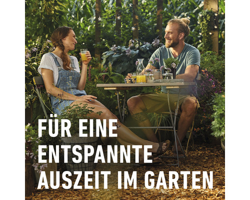 Mann und Frau entspannen sich im Garten mit Getränken an einem Tisch.