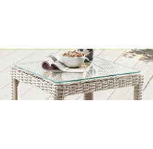 Gartentisch mit Glasplatte und Rattanstruktur, darauf liegen eine Zeitschrift, eine Schale mit Snacks und eine Tasse