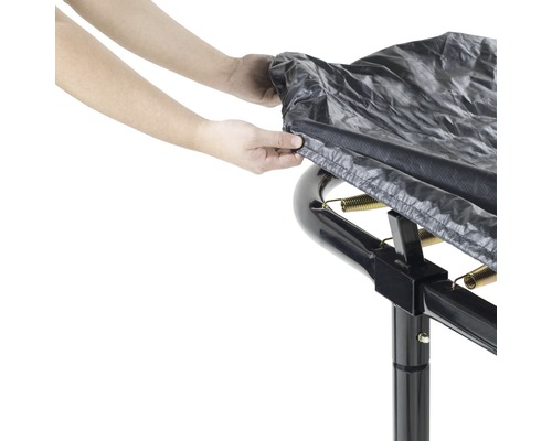 Person befestigt eine Schutzhülle auf einem Gartentrampolin.