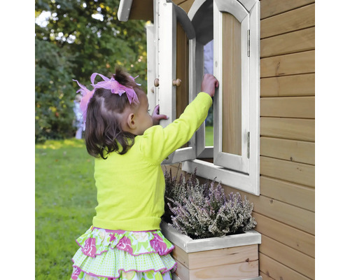 Ein Kind öffnet ein Fenster an einem Holzspielhaus mit Blumenkasten.