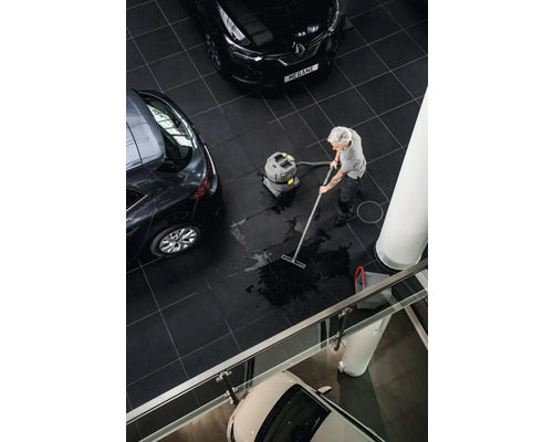 Eine Person reinigt einen Fliesenboden mit einem Nass Trockensauger in einem Ausstellungsraum mit Autos.