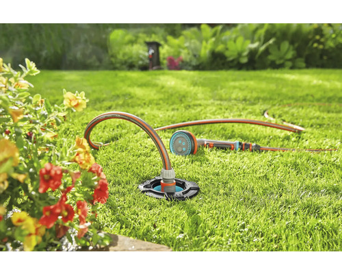 Gartenszene mit einem versenkten Rasensprenger und einem Gartenschlauch auf einer Rasenfläche.