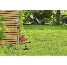 Gartenszene mit Wasserhahn, Gartenschlauch und Rasensprenger zur Bewässerung