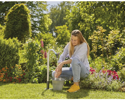 Eine Frau wäscht sich die Hände an einem Gartenwasserhahn mit Eimer im Garten.
