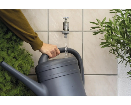 Person füllt eine Gießkanne mit Wasser aus einem Wasserhahn im Garten