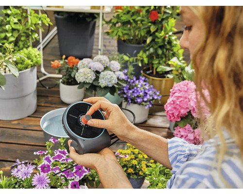 Frau bedient Gardena Solar Bewässerungsset mit Blumen im Hintergrund