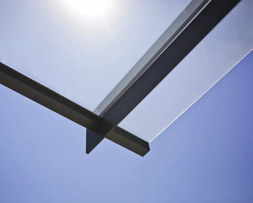 Detailaufnahme eines Glasvordachs mit Metallrahmen vor blauem Himmel