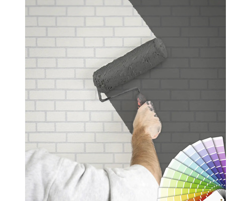 "Eine Person streicht eine Ziegelwand mit einer Farbrolle