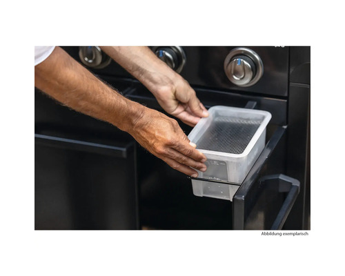 Person setzt eine Wasserschale in einen Gasgrill.