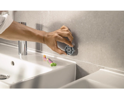 Person befestigt Badaccessoire an Wandfliesen im Badezimmer.