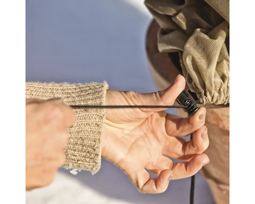 Eine Person zieht den Kordelzug an einer Pflanzenschutzhülle fest.