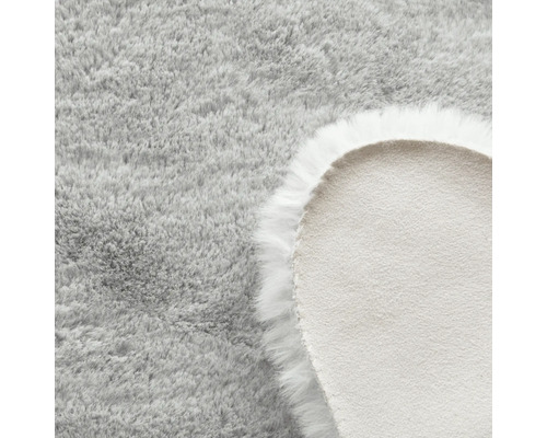 Detailansicht eines runden, hellgrauen Teppichs mit langem Flor