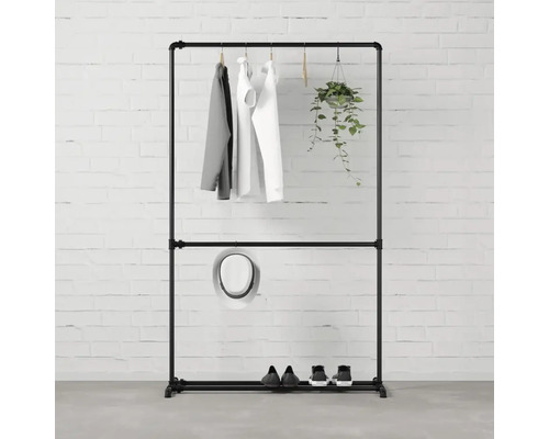 Schwarzer Kleiderständer mit Kleidung, Hut, Schuhen und hängender Pflanze vor einer Backsteinmauer.