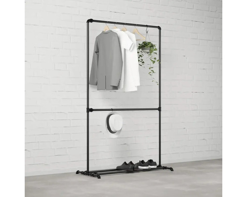 Schwarzer Kleiderständer mit Kleidung, Hut, Schuhen und Pflanze vor einer Ziegelwand