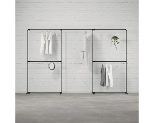 Schwarzes, modulares Kleiderständer-System mit Kleidung und Dekoration vor einer Ziegelwand