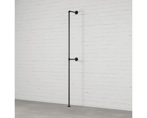 Schwarzer Kleiderständer aus Metallrohr an einer weißen Backsteinmauer