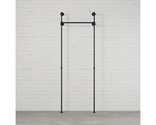 Schwarzer Kleiderständer aus Metallrohren vor einer weißen Ziegelwand