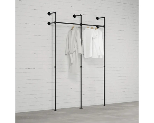 Schwarze Kleiderstange mit Kleidung vor einer Ziegelwand