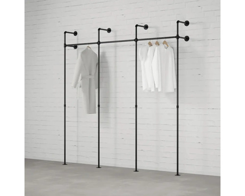 Schwarzes Kleiderständer-System aus Rohren mit hängenden Kleidungsstücken vor einer Ziegelwand