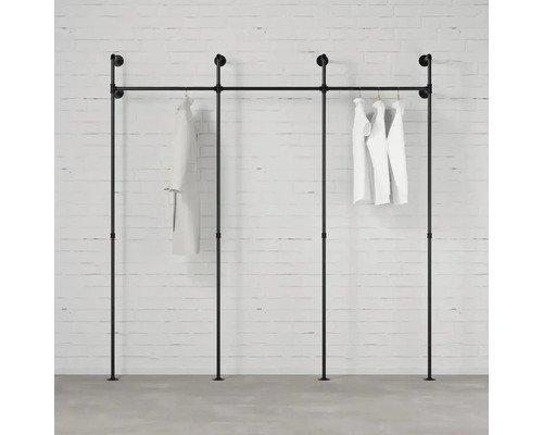 Schwarzer Kleiderständer aus Rohren mit weißer Kleidung an einer Ziegelwand