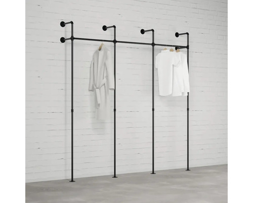 Schwarze Kleiderständer-Kombination aus Rohren vor einer weißen Ziegelwand mit hängenden Kleidungsstücken.