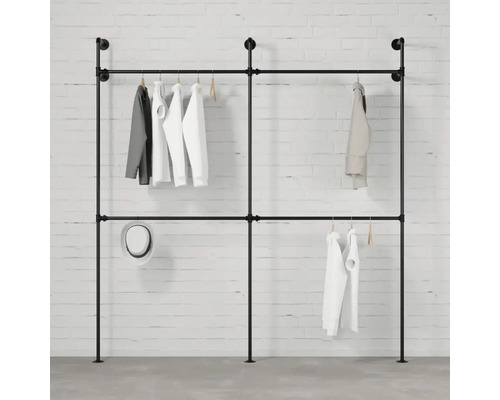 Freistehende Kleiderstange aus Rohren mit daran aufgehängter Kleidung vor einer weißen Ziegelwand.