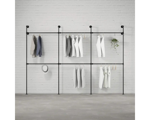 Schwarzer Kleiderständer aus Metallrohren mit Kleidung vor einer Ziegelwand