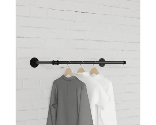 Wandgarderobe aus Metallrohr mit Kleidung an Holzbügeln vor einer Backsteinwand