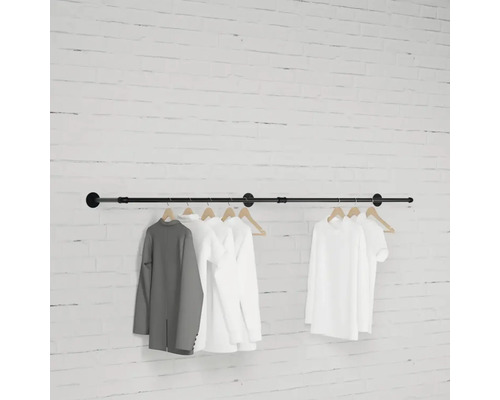 Schwarze Kleiderstange mit daran hängenden Kleidungsstücken vor einer Backsteinwand