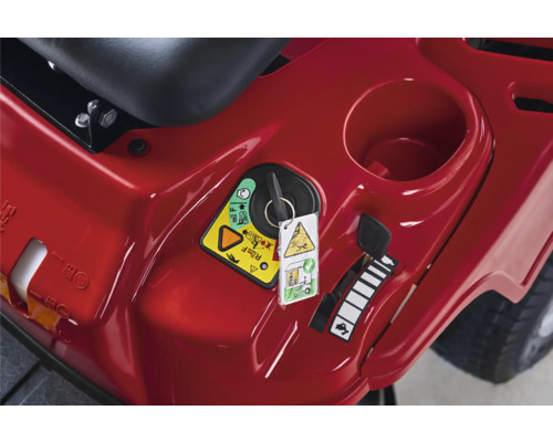 Nahaufnahme des Armaturenbretts eines Rasentraktors mit Zündschloss, Sicherheitshinweisen und Geschwindigkeitsregler.