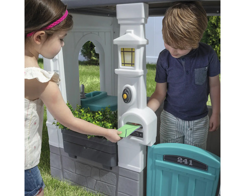 Kinder spielen mit einem Spielhaus mit Briefkasten und Spüle
