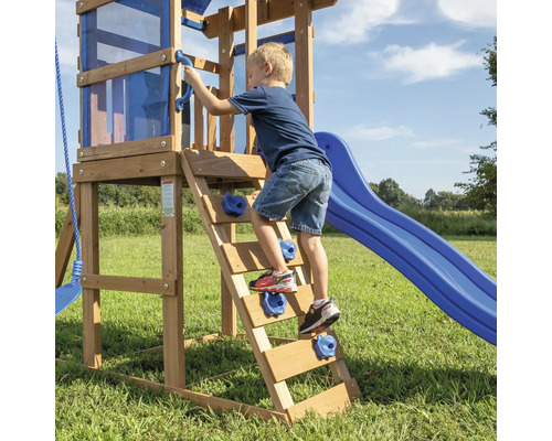 Junge klettert auf einem Spielturm mit Rutsche und Kletterwand aus Holz.