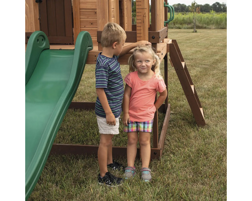 Zwei Kinder stehen neben einem Spielplatzgerät mit Rutsche und Leiter im Garten.