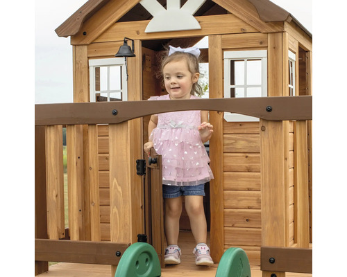 Mädchen steht im hölzernen Spielhaus mit Tür und Fenster