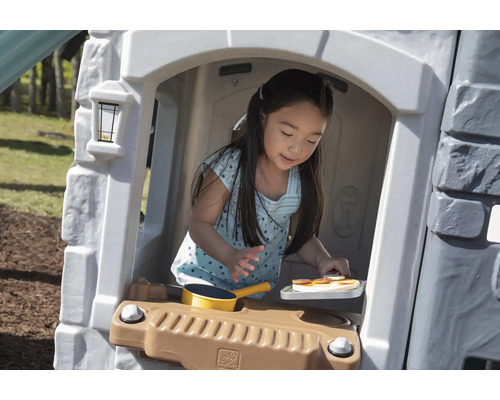 Mädchen spielt in einem Spielhaus mit Spielküche im Garten