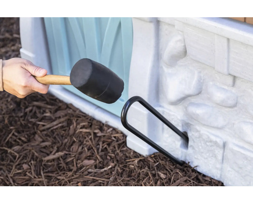 Ein Gummihammer wird verwendet, um eine schwarze Metallstange in ein Spielhaus einzutreiben.