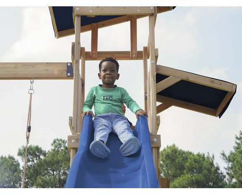 Junge auf einer blauen Rutsche eines Spielturms aus Holz