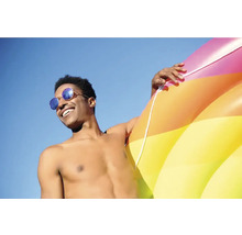 Mann mit Sonnenbrille und aufblasbarem Schwimmreifen vor blauem Himmel