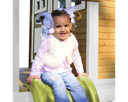 Ein Mädchen sitzt auf einer Rutsche vor einem Holzspielhaus.