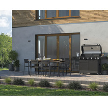 Terrasse mit Grill, Tisch und Stühlen vor einem Haus.