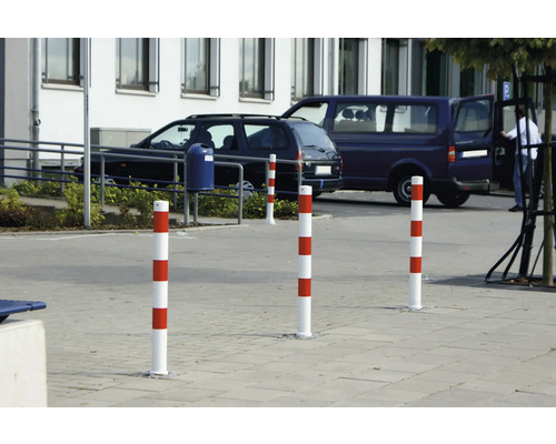 Mehrere rot-weiß gestreifte Absperrpfosten auf einem Parkplatz.