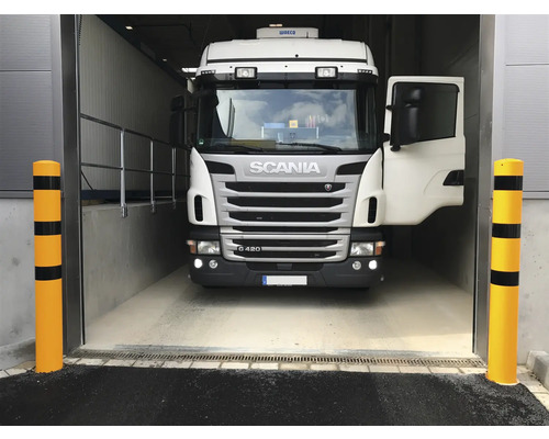 Ein Lastwagen fährt in ein Lagerhaus ein, geschützt durch gelbe Anfahrschutzpfosten.
