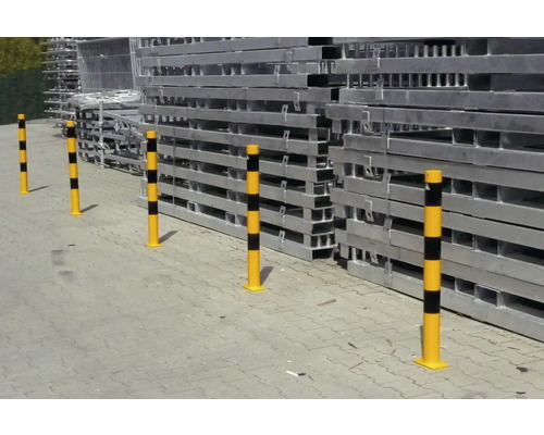 Mehrere gelbe Anfahrschutzpfosten mit Streifen vor einem Stapel von Baugerüstteilen