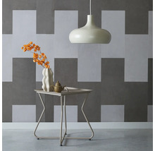 Innenaufnahme mit Pendelleuchte, Tisch mit Blumenvase und Teekanne vor einer geometrischen Wand