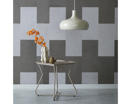 Innenaufnahme mit Pendelleuchte, Tisch mit Blumenvase und Teekanne vor einer geometrischen Wand
