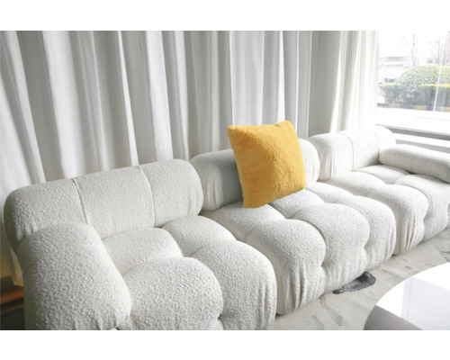 Modulares Sofa mit gelbem Kissen vor einem Fenster mit Vorhängen.