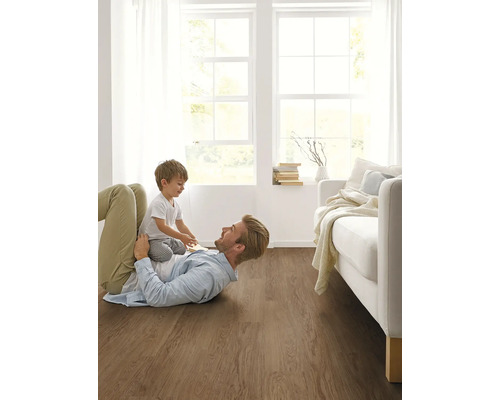 Vater und Kind spielen auf einem Bodenbelag aus Holz in einem hellen Wohnzimmer.